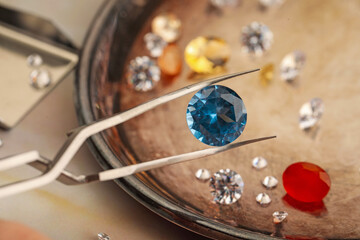 Tweezers with beautiful gemstones on light table, selective focus