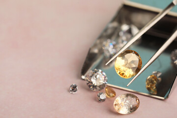 Tweezers with beautiful gemstones on light pink table, selective focus. Space for text