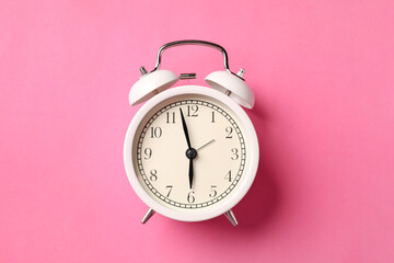 White alarm clock on pink background, top view