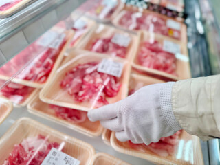 スーパーマーケットのお肉のパックを手に取る白手袋をした女性