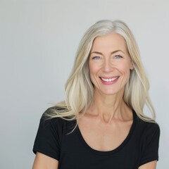 A woman with long, light blonde hair smiles warmly while wearing a simple black top against a light-colored background, radiating positivity