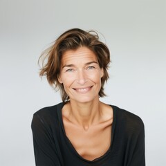 Obraz premium A middle-aged woman with a warm smile and tousled hair poses against a light backdrop, radiating confidence and joy