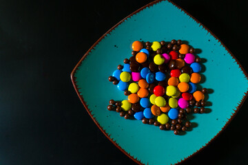 Close-up of colorful chocolate candies on a vibrant turquoise plate, perfect for food and confectionery themes