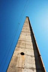 Tall concrete chimney reaching into a clear blue sky with power lines