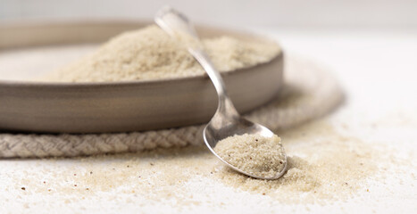 Raw uncooked fonio seeds on a plate with a metal spoon on white table. African ancient pseudocereal