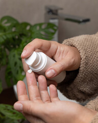 Woman in brown bathrobe pumping cream on finger and holding a cosmetic bottle in bathroom