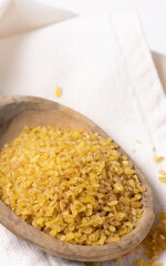 Raw dry uncooked yellow bulgur grain in a wooden bowl on white table cloesup. Ancient food
