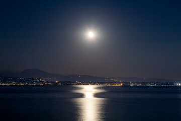 Full moon over Lake Garda at night, casting a shimmering reflection on the calm waters of Sirmione, Italy