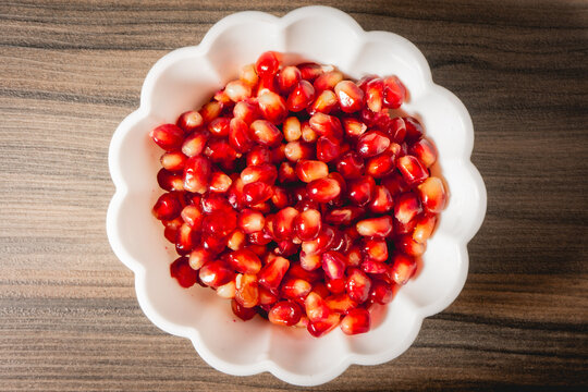 A white bowl with seeds of Pomegrenade, on a wooden background.