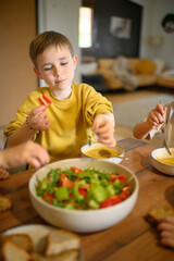 A young boy enjoys a healthy meal with his family, eating soup and salad with great appetite. The scene reflects wholesome nutrition, warmth, and togetherness at the dining table.