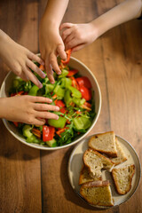 Small children’s hands reach for fresh vegetables from a shared salad bowl on the table. A colorful and healthy meal encourages kids to enjoy fresh food together.