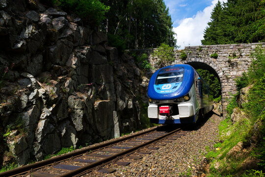 NEJDEK, CZECH REPUBLIC - JULY 23: Ceske drahy CD railway carrier company train passes under romantic stone bridge in beautiful forest in Ore Mountains on July 23, 2017 in Nejdek, Czech Republic.
