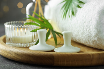Spa stones, burning candle, towel and green leaves on grey table, closeup