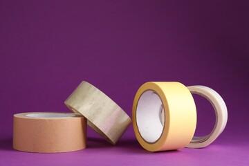Rolls of different adhesive tapes on purple background