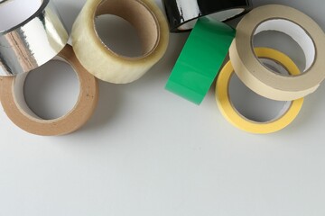 Rolls of different adhesive tapes on white background, flat lay. Space for text