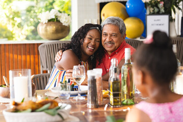 Multiracial family celebrating retirement, daughter hugging father at dinner table, in garden