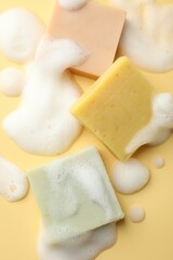 Soap bars with foam on yellow background, flat lay