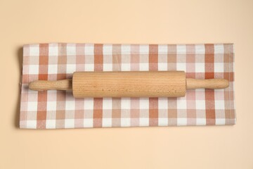 Wooden rolling pin and checkered napkin on beige background, top view