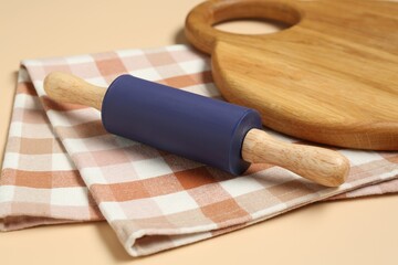 Rolling pin, wooden board and checkered napkin on beige background, closeup