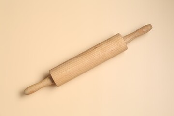 Wooden rolling pin on beige background, top view