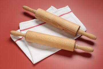 Wooden rolling pins and napkin on red background, above view