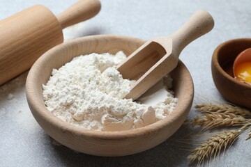 Flour in bowl, spikes, rolling pin and yolk on light grey table, closeup