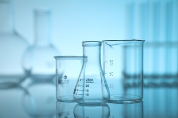 Laboratory glassware on mirror surface against light blue background