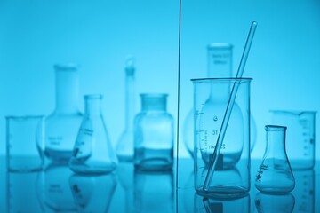 Laboratory glassware on mirror surface against light blue background