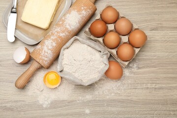 Rolling pin and different ingredients on light wooden table, flat lay