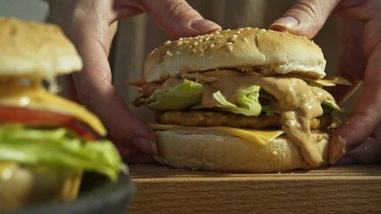 Chef prepares delicious burger by placing sesame bun on top and pressing it so that delicious sauce made from mayonnaise and ketchup flows out of hamburger. Close up.