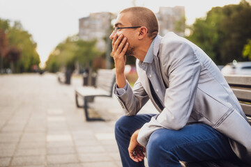 Portrait of thoughtful and worried man. He is sitting on bench in the city and thinking after getting fired at work.
