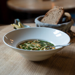 Traditionelle Pfannkuchensuppe mit klarer Rinderbrühe, Pfannkuchenstreifen und frischen Kräutern, serviert im Wirtshaus mit Brotkorb und Butter

