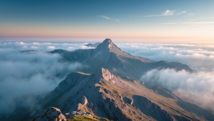 Mountain landscape with peaks rising above clouds during sunset in a clear sky with soft light and shadows in the foreground.