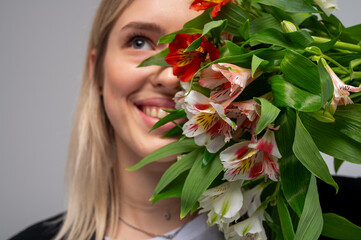 Fototapeta premium Smiling woman with bouquet of fresh alstroemeria flowers. Close-up portrait with bright petals and green leaves. Natural beauty, joy and floral elegance, selective focus