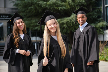 Happy graduates posing outdoors in academic regalia