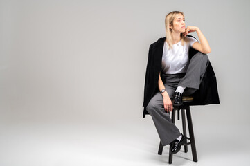 Smiling young woman in stylish business casual outfit sitting on stool on neutral background....