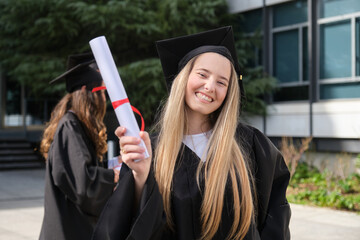 Happy graduating student holding diploma celebrating graduation day near university