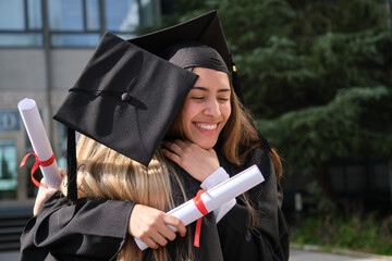 Two female graduates hugging each other, holding their diplomas and celebrating their graduation