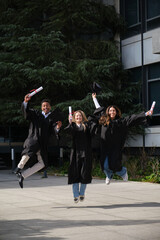 Group of cheerful graduated students jumping together holding their diplomas on graduation day