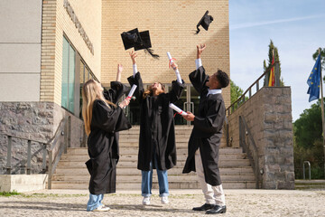 Group of cheerful multi ethnic graduates throwing graduation caps in the air after graduation...