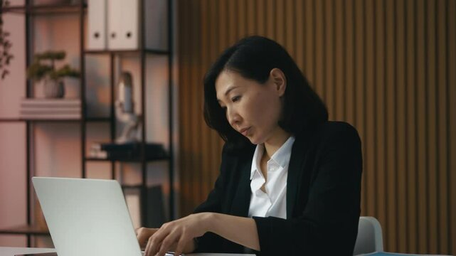 Asian female manager types on laptop while handling a complaint from a client