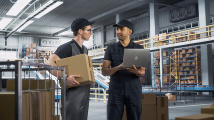 Multiethnic Male Manager Talking To Caucasian Warehouse Worker In Modern Sorting Center Facility With Conveyor Belt. Two Man Using Laptop Computer To Fulfil Customer Orders And Deliver Packages.