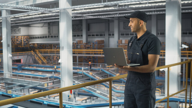 Logistics Transportation Warehouse Facility: Associate Worker Uses Laptop in Retail Distrubution Center, Controls Efficiency of Conveyor Loading Online Ordered Product Boxes for Delivery to Customers