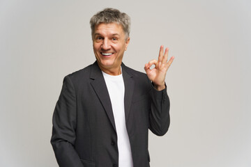 Man in a blazer making an okay gesture, showcasing a cheerful expression against a neutral...
