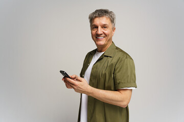 Smiling man holding smartphone while standing indoors against a neutral background