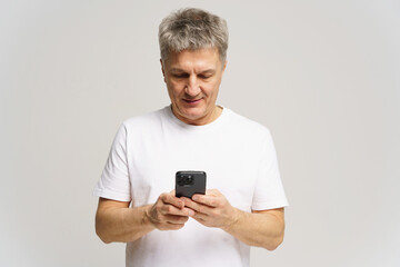 Man in white t-shirt engages with smartphone, focused on activity, indoors, casual setting