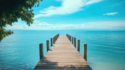 Fototapeta premium A beautiful wooden pier reaching toward a sparkling sea, surrounded by peaceful nature and a bright blue sky.