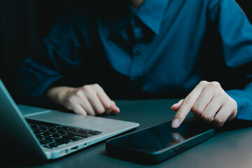 Woman in Blue Shirt Using Smartphone Next to Laptop on Table