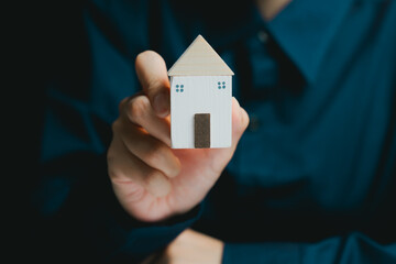 Small Wooden House Model Held by Person in Dark Shirt