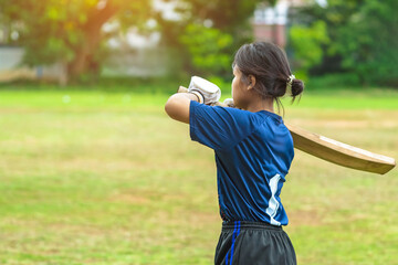 Asian young female cricket player wear protective gear and hitting ball with bat on field. Woman teenager playing cricket in park. Girl with bat and ball on cricket pitch. Sports activity and exercise